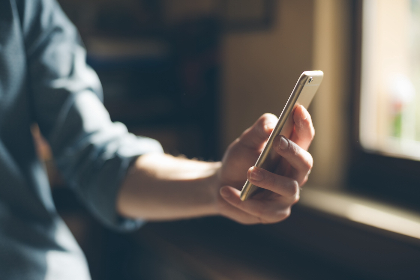 Detail of a person’s arm dressed in casual work clothes holding a smartphone, representing mobile device management (MDM) capabilities